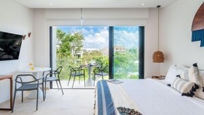 A modern bedroom with a bed, a desk, and chairs, a ceiling fan, and a large window with a view of greenery and buildings. - BPH04 CPL, Luxury estudio PH con piscina privada (Tulum)