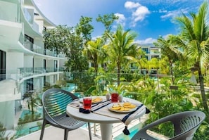 A balcony with a table set for two, surrounded by lush greenery and a clear blue sky. - A212 CPL, Luxury Studio Lagoon View (Tulum)