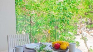 Mesa posta com pratos, talheres, uma saladeira e um vaso de flores, com vista para o verde lá fora.