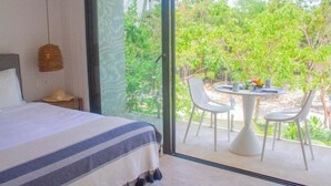 Quarto com uma janela grande, cama com colcha listrada e área de refeições com mesa e cadeiras.