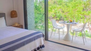 Une chambre avec une grande fenêtre, un lit recouvert d’une courtepointe à rayures et un balcon avec une table et des chaises.
