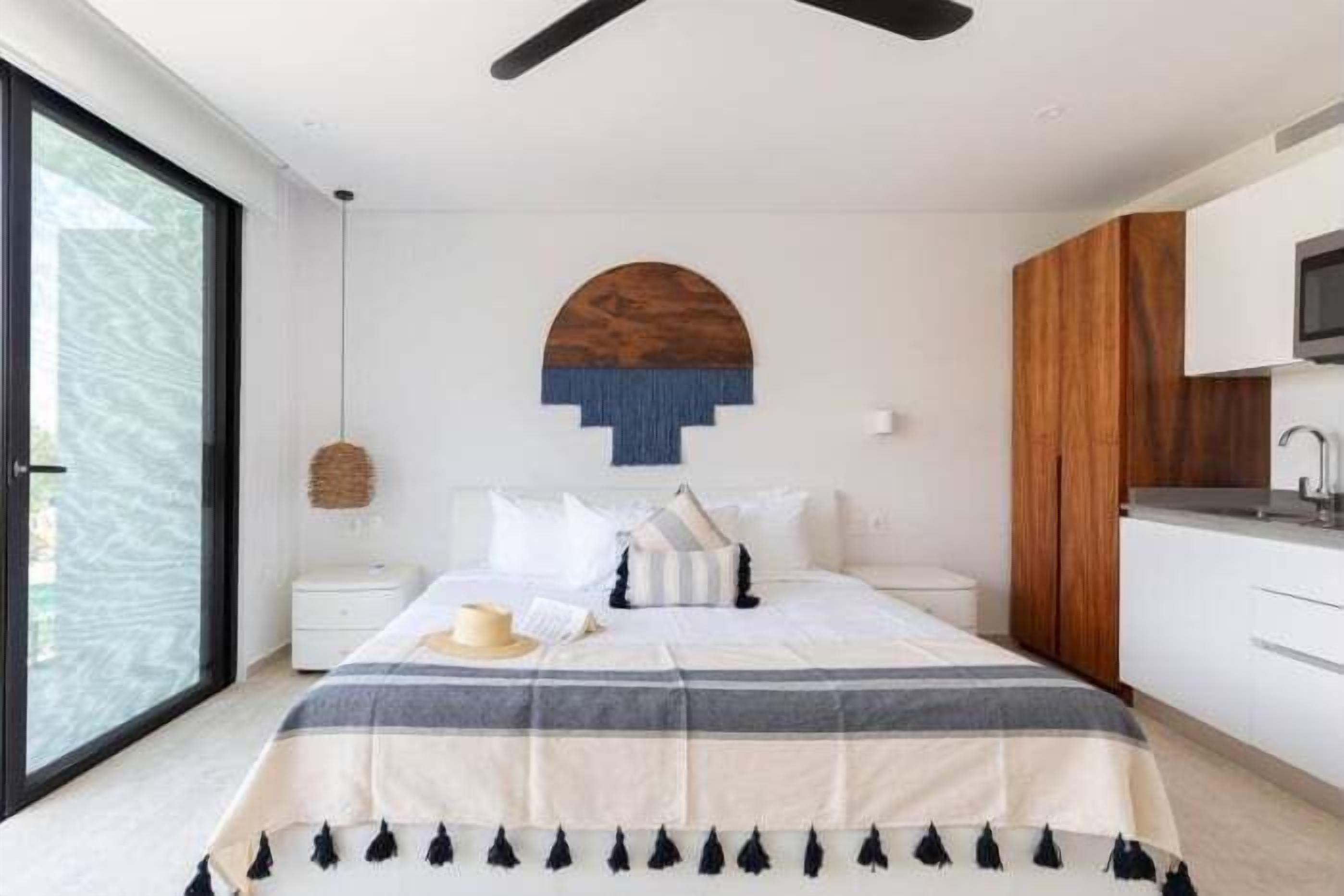 A modern bedroom with a large bed, a wooden accent wall, a hanging light, and a view through a large window.