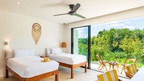 A modern hotel room with two beds, a ceiling fan, a large window with a view of greenery, and a small table with chairs. - B203 CPL, Grandioso estudio con air conditioning (Tulum)