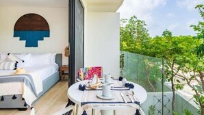A bedroom with a bed, a bedside table, and a window overlooking a balcony with a view of greenery. - B205 CPL, Amazing air conditioned studio (Tulum)