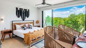 Quarto moderno com uma cama grande, cabeceira de madeira e vista para o verde através de grandes janelas.