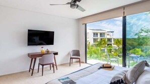 Una moderna camera d'albergo con un letto, una scrivania, una sedia, una TV e un balcone con vista sul verde.
