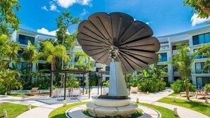 A modern building with a large, metallic sculpture in the center of a courtyard surrounded by greenery and outdoor seating areas. - B409 CPL, Studio Jungle View-No Air Conditioning (Tulum)