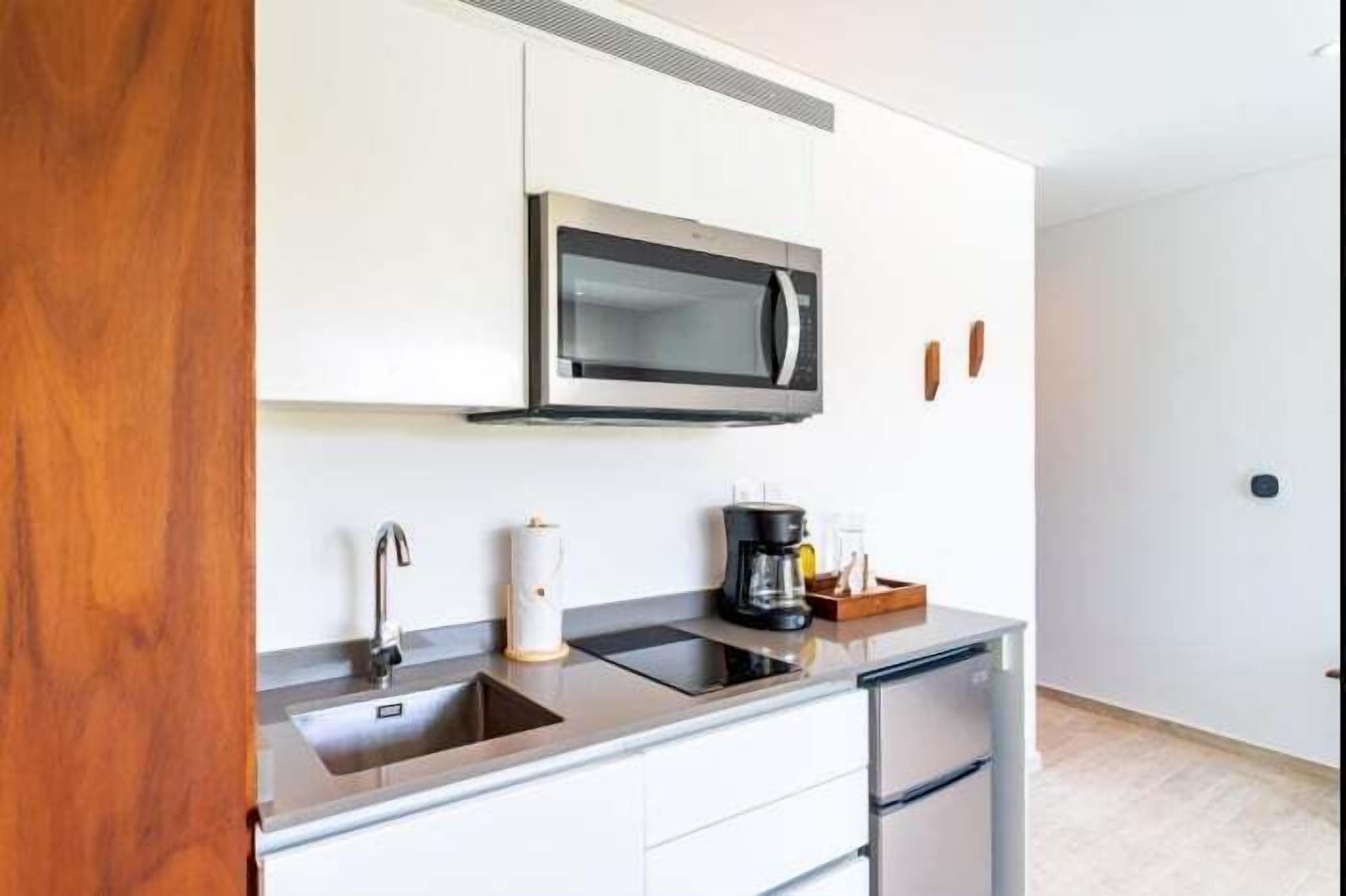 Een moderne keuken met een ingebouwde magnetron, een RVS spoelbak en een koffiezetapparaat op het aanrecht.