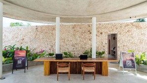 Un espace extérieur aménagé avec des sièges, abrité par un toit, avec un mur en pierre en arrière-plan, deux chaises en bois et une table sur laquelle se trouve un ordinateur portable.