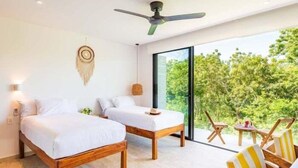 Un dormitorio moderno con un ventanal grande, dos camas, un ventilador de techo y una pequeña mesa con sillas.