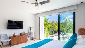 A modern bedroom with a bed, a TV, a desk, and a large window with a view of greenery. - D202 CPL, Gym|Spa|Coworking (Tulum)