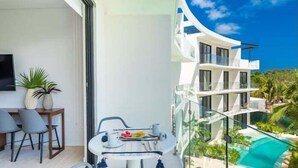 Un balcon moderne avec une balustrade en verre donnant sur une piscine et un bâtiment blanc doté de nombreux balcons.