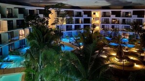 Un resort con diverse piscine, palme e un edificio moderno con balconi.