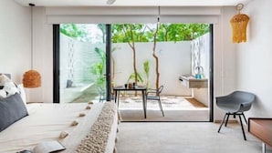 A modern bedroom with a bed, a ceiling fan, a dining area with a table and chairs, and a view of the outdoors. - A107 CPL, Magnifico Studio Garden Jungle View (Tulum)