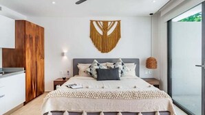A modern bedroom with a bed, bedside tables, a ceiling fan, and a large window. - A107 CPL, Magnifico Studio Garden Jungle View (Tulum)