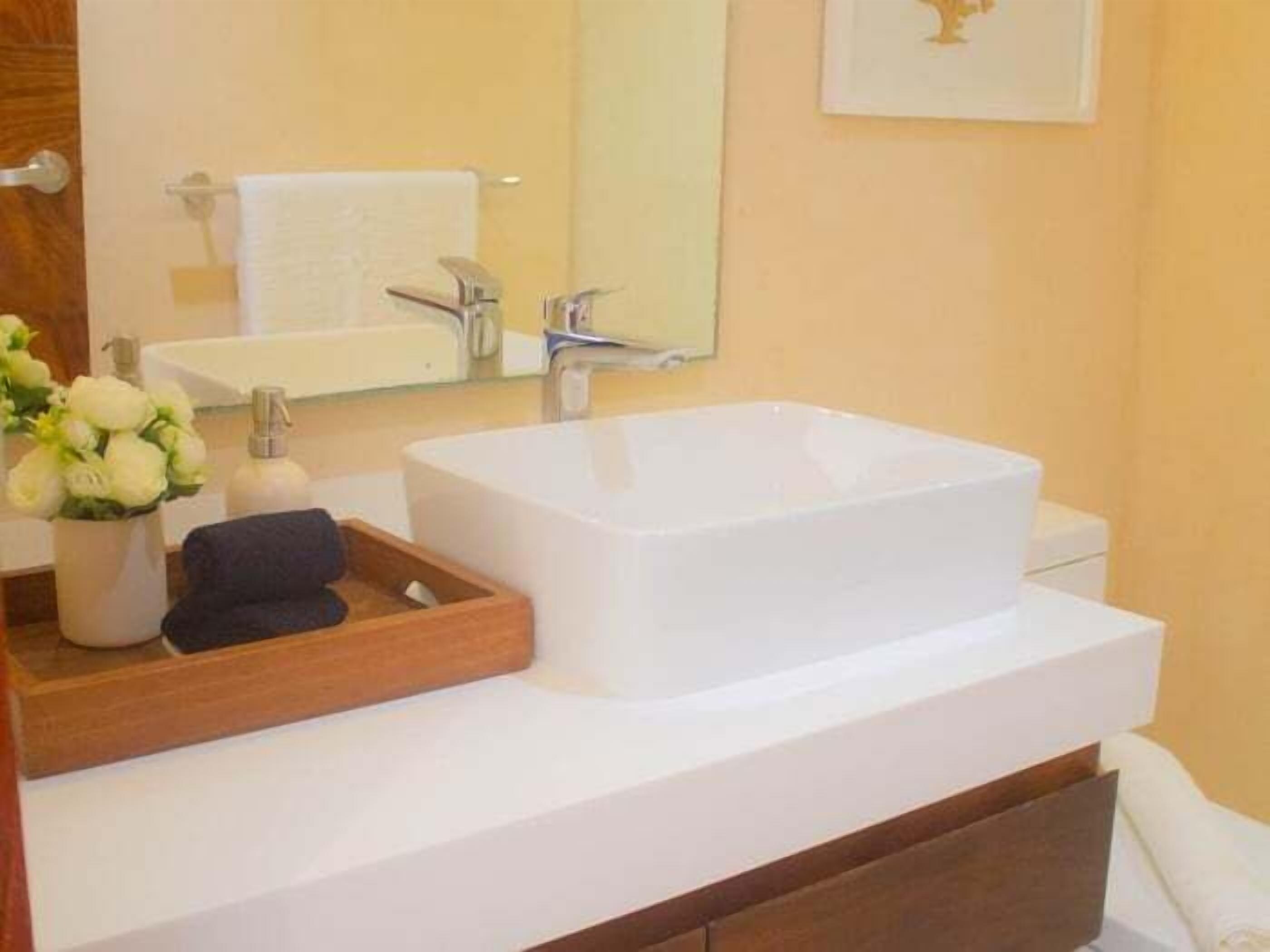 A bathroom with a white sink, a mirror, and a wooden tray with flowers.