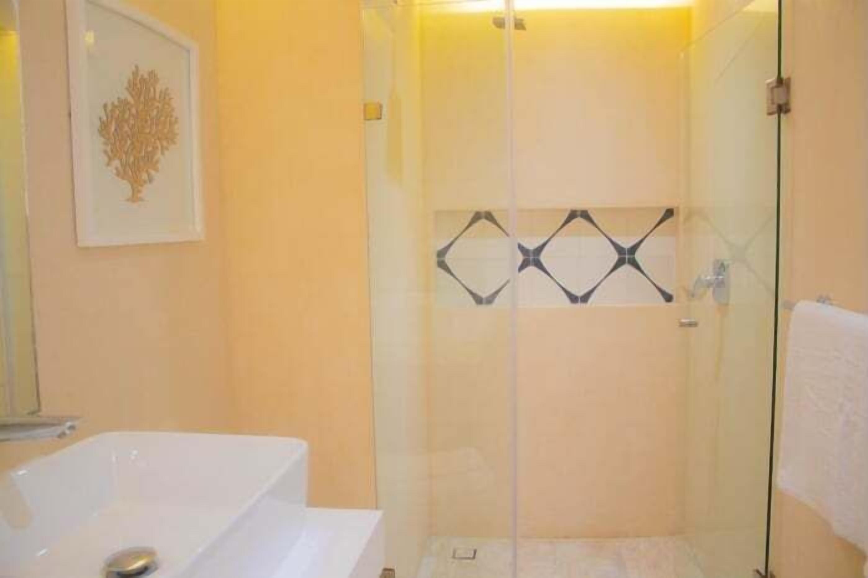 A bathroom with a glass-enclosed shower, a white bathtub, and a framed artwork on the wall.