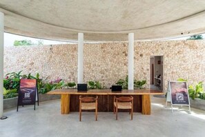 Ein Sitzbereich im Freien mit Stehwänden, einem Holztisch und zwei Korbstühlen.