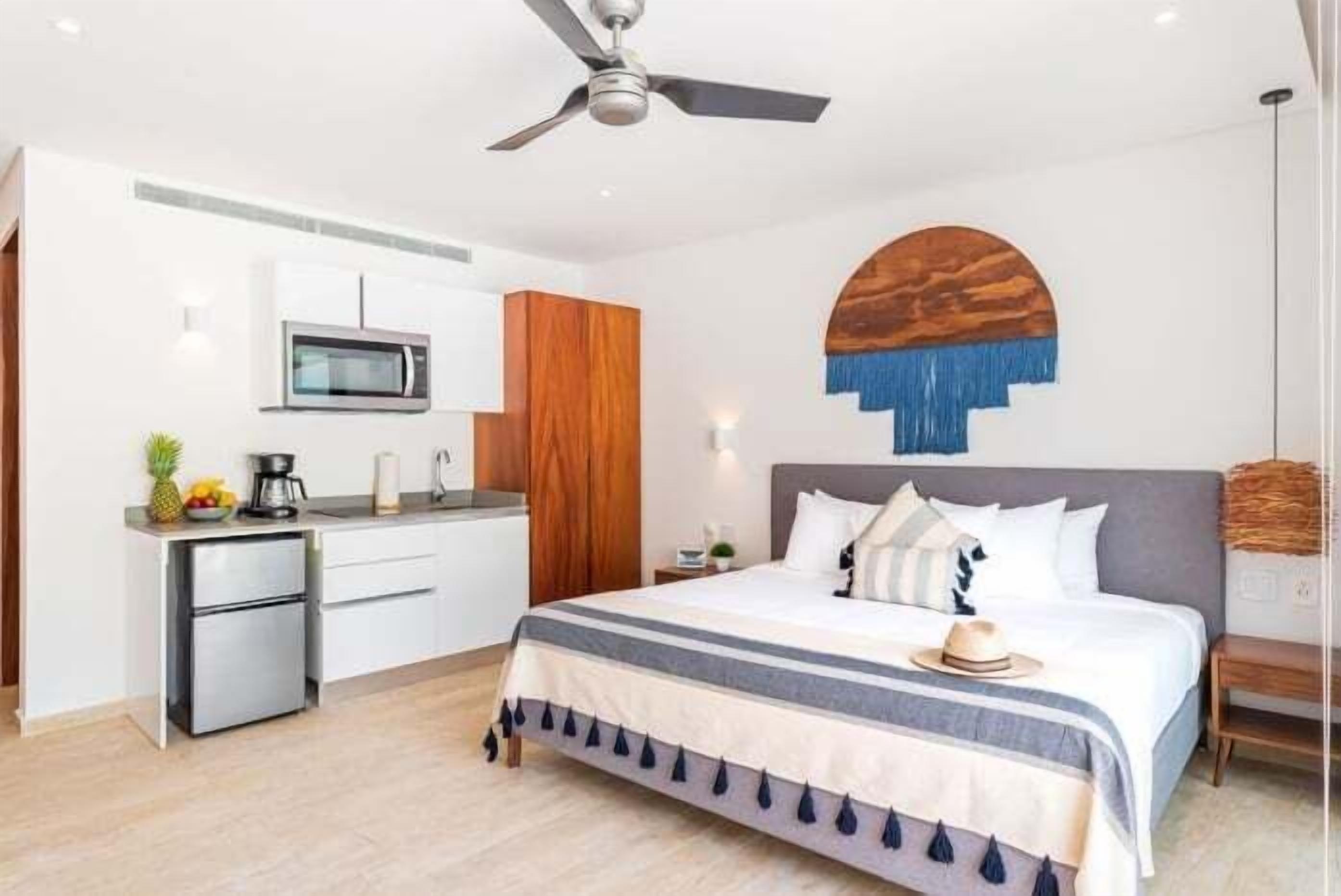 Una habitación de hotel moderna con una cama, kitchenette y un ventilador de techo.