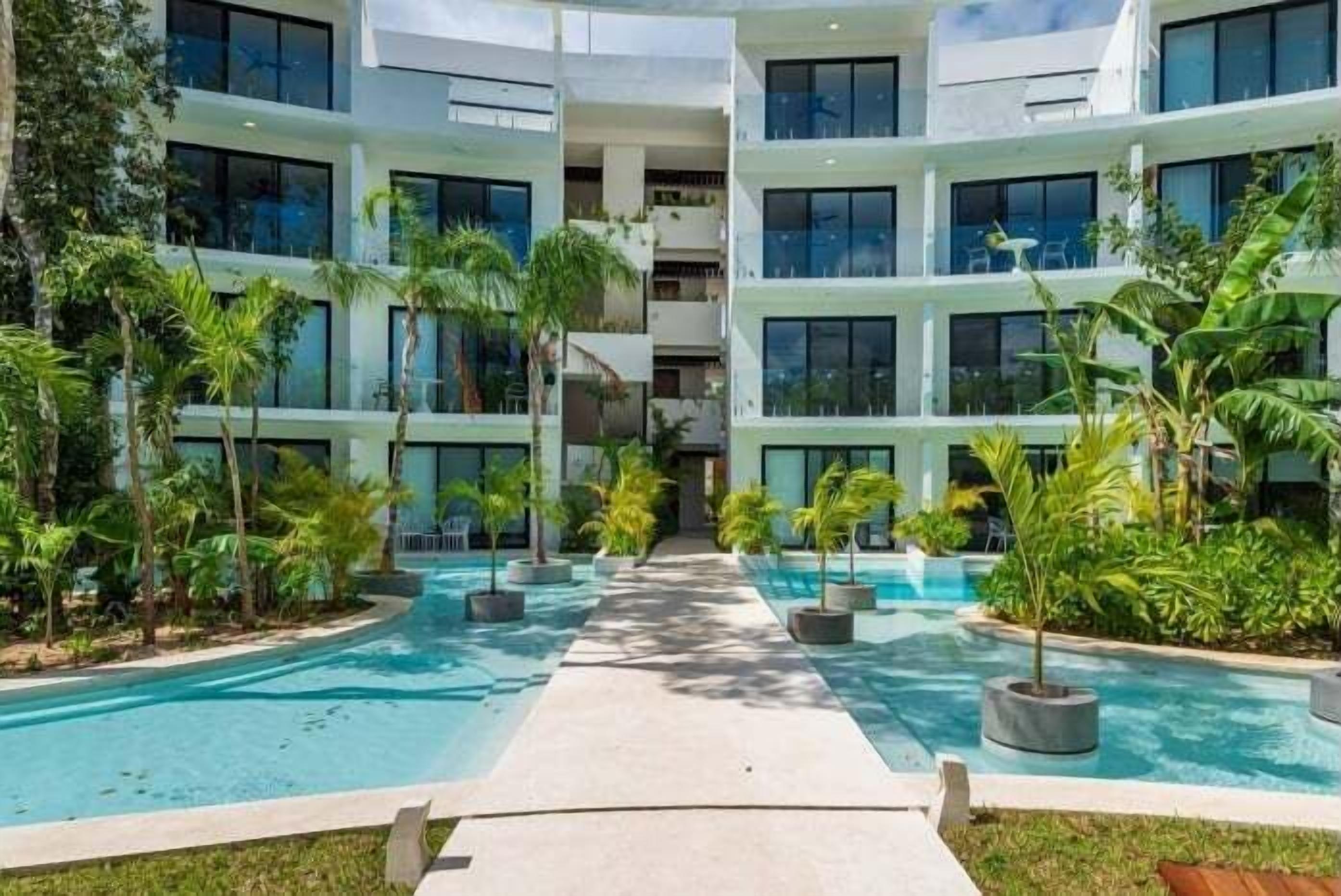 A modern hotel with a central pool, surrounded by lush greenery and multiple balconies.