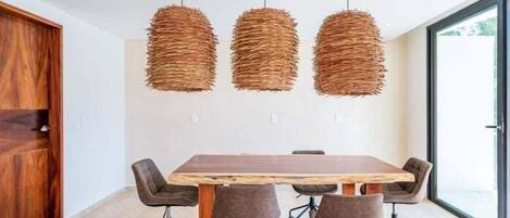 A conference room with a wooden table and six chairs, three hanging wicker pendant lights, and a large window.