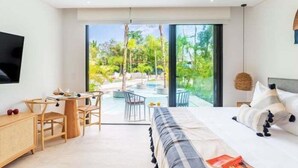 Camera d'albergo moderna con un letto grande, una scrivania e vista su un giardino tropicale e una piscina.