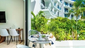 Moderni hotellihuone, jossa on ruokailutila, televisio ja parveke, jolta avautuu näkymä vehreään maisemaan.