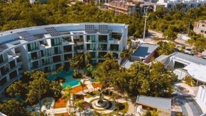 A modern hotel with a circular pool surrounded by lush greenery and solar panels on the roof. - E102 CPL, Comfortable Swim Up Studio (Tulum)