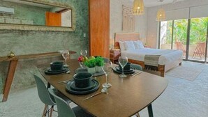 Ett modernt hotellrum med en matplats, en stor säng och en balkong med utsikt över grönområden.