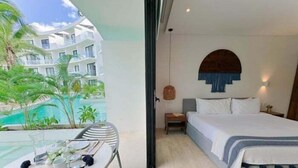 Hotelkamer met een bed, een klein tafeltje met stoel, uitzicht op een zwembad en een balkon met planten.