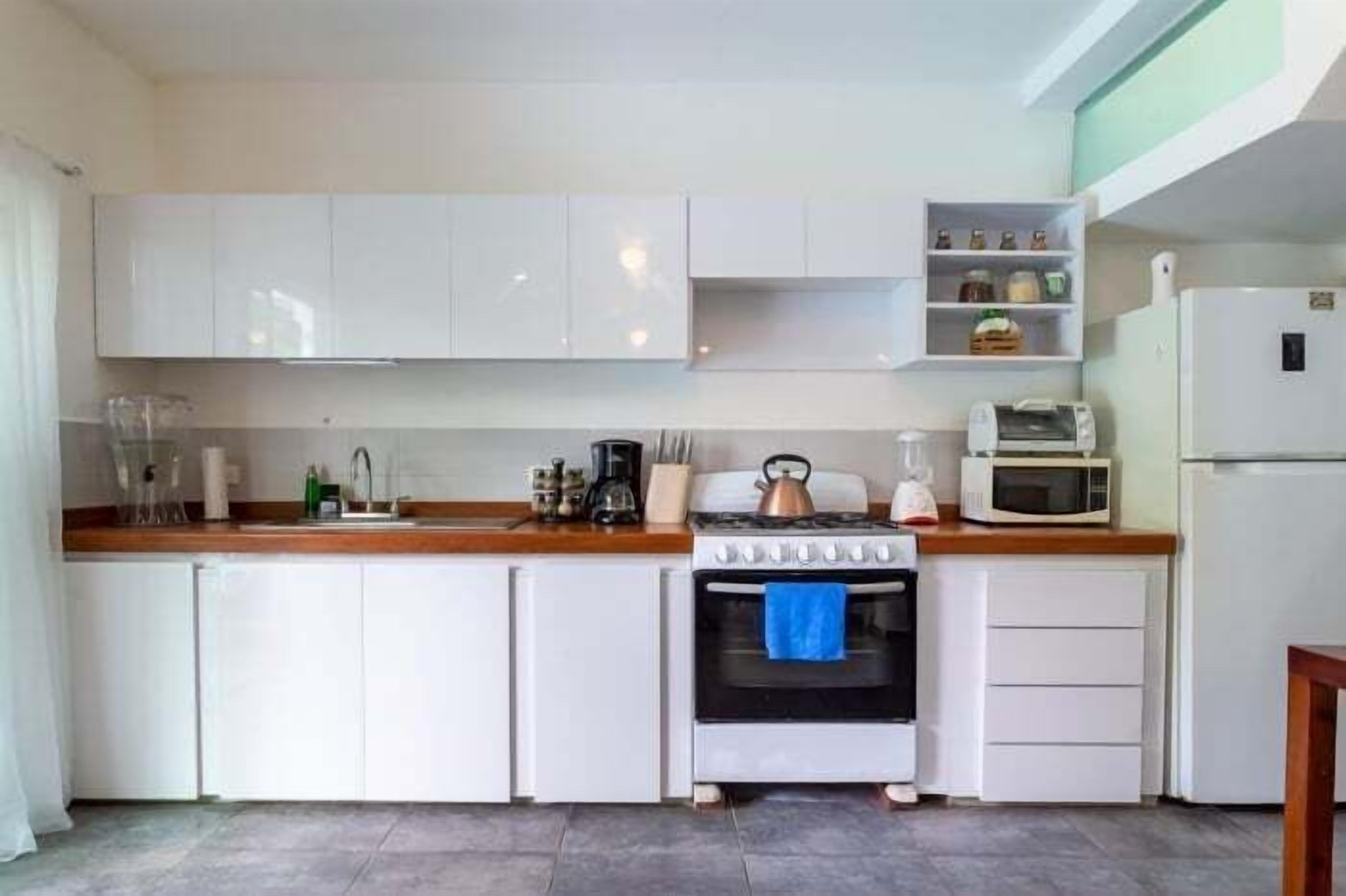 A compact kitchen with white cabinets, a stove, a microwave, and a refrigerator.