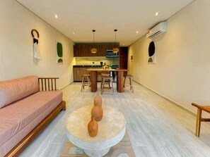 A modern living room with a sofa, a round coffee table with vases, a kitchen in the background, and a dining area with stools. - Dk Jade 3, Your Exclusive Refuge in Tulum (Tulum)