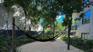 A gravel path leading to a hammock under trees, surrounded by greenery and modern buildings. - IIK C409, Luxury Studio/private individual pool (Tulum)