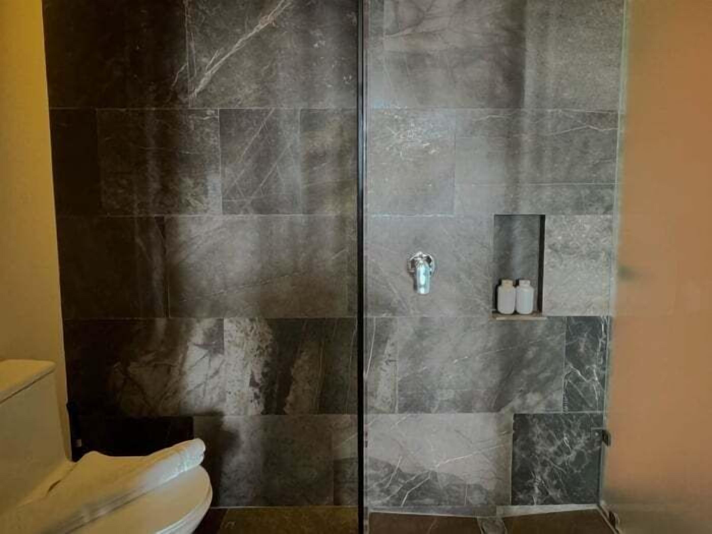 Un baño con cabina de ducha de vidrio, baldosas de mármol y un pequeño estante con artículos de aseo.
