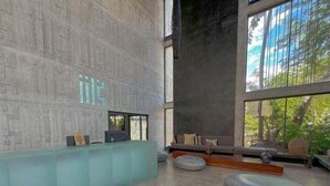 A spacious lobby with a modern design, featuring a reception desk, seating area, and large windows offering a view of greenery outside. - IIK C409, Luxury Studio/private individual pool (Tulum)