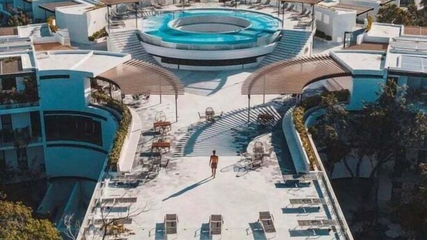 Ett modernt hotell med en pool i mitten, solstolar och ett avskärmat sittområde.