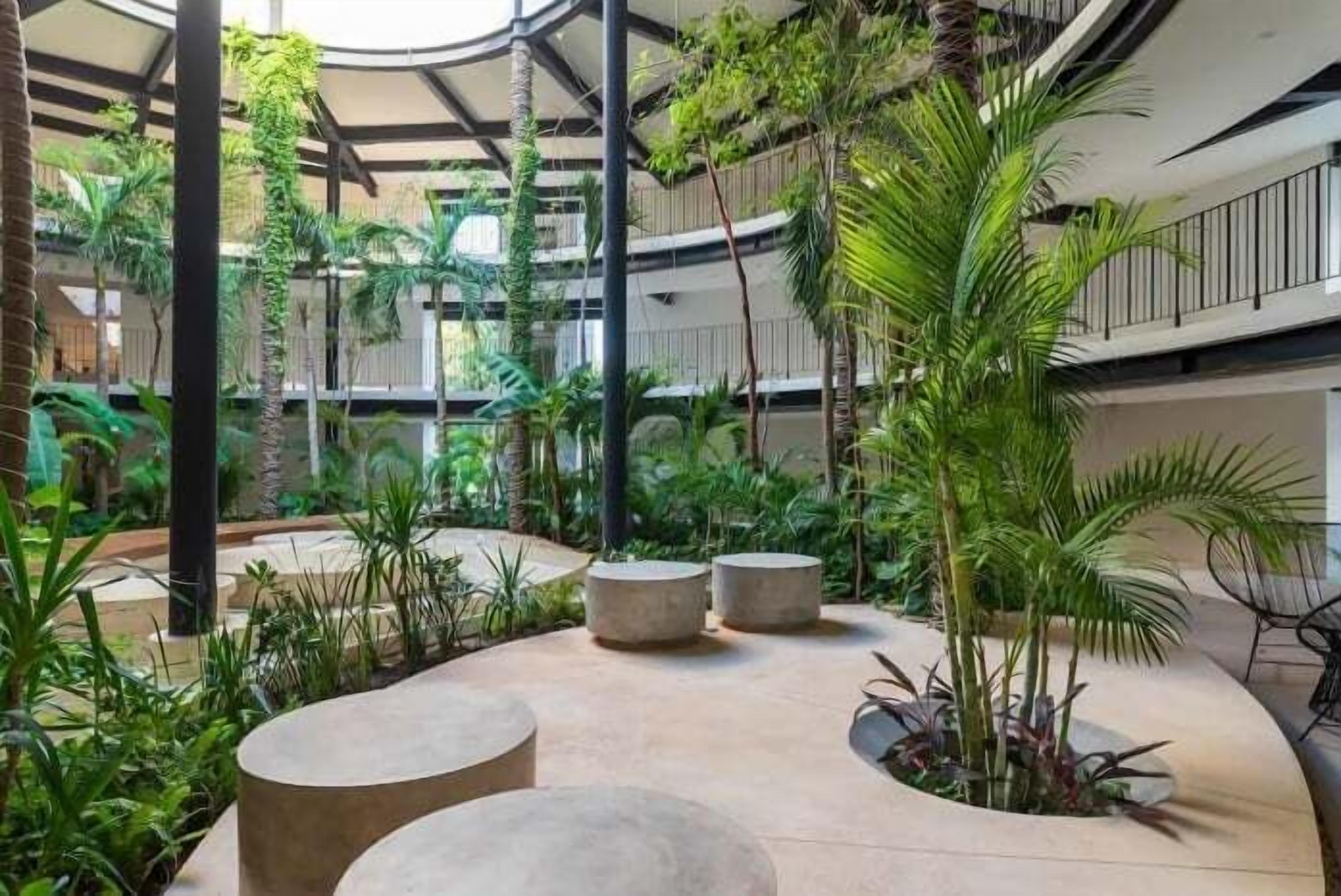 Um átrio de vários níveis com uma área de estar circular central, rodeado por vegetação exuberante e plantas.