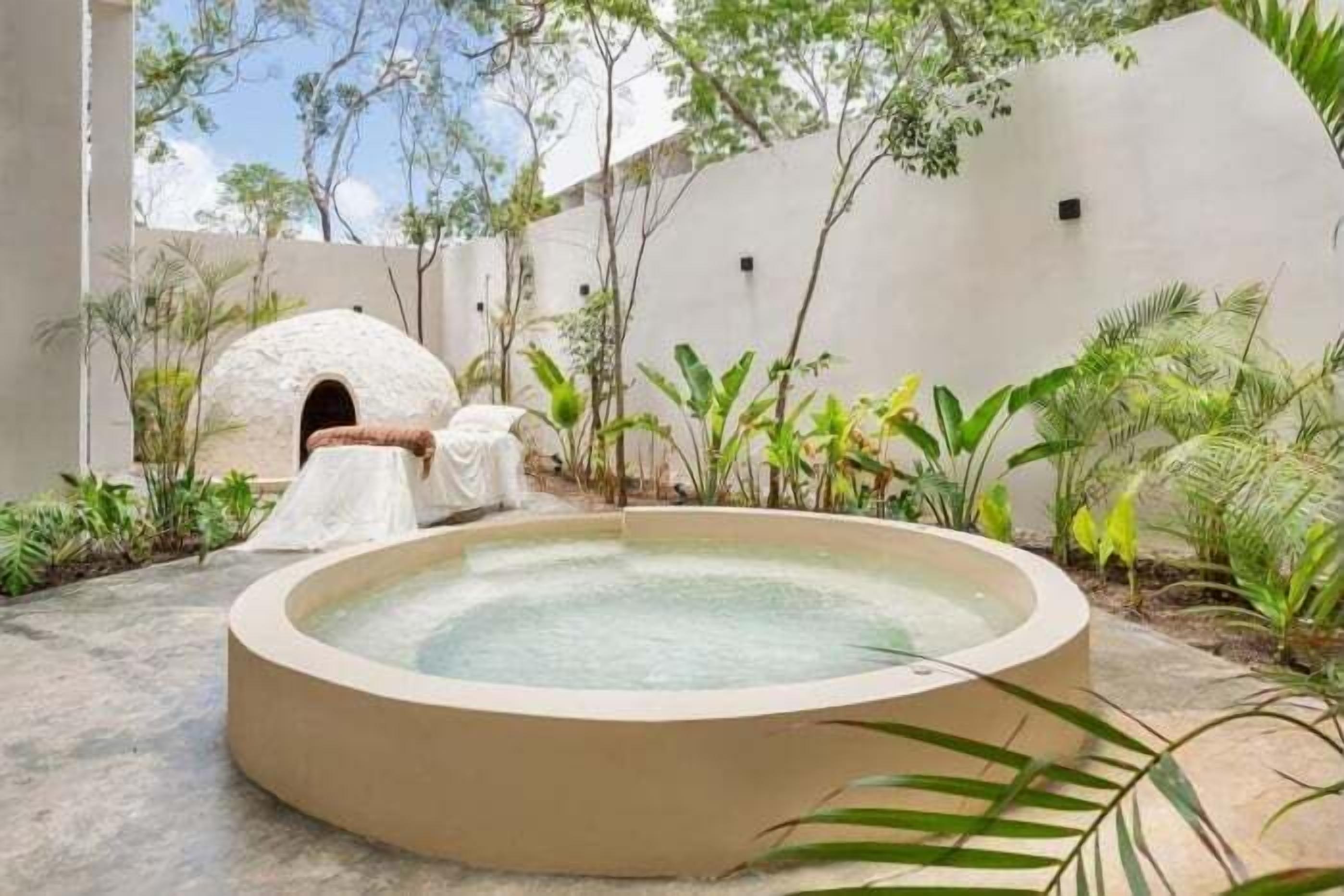 A circular hot tub in a courtyard with a dome-shaped structure and lush greenery.