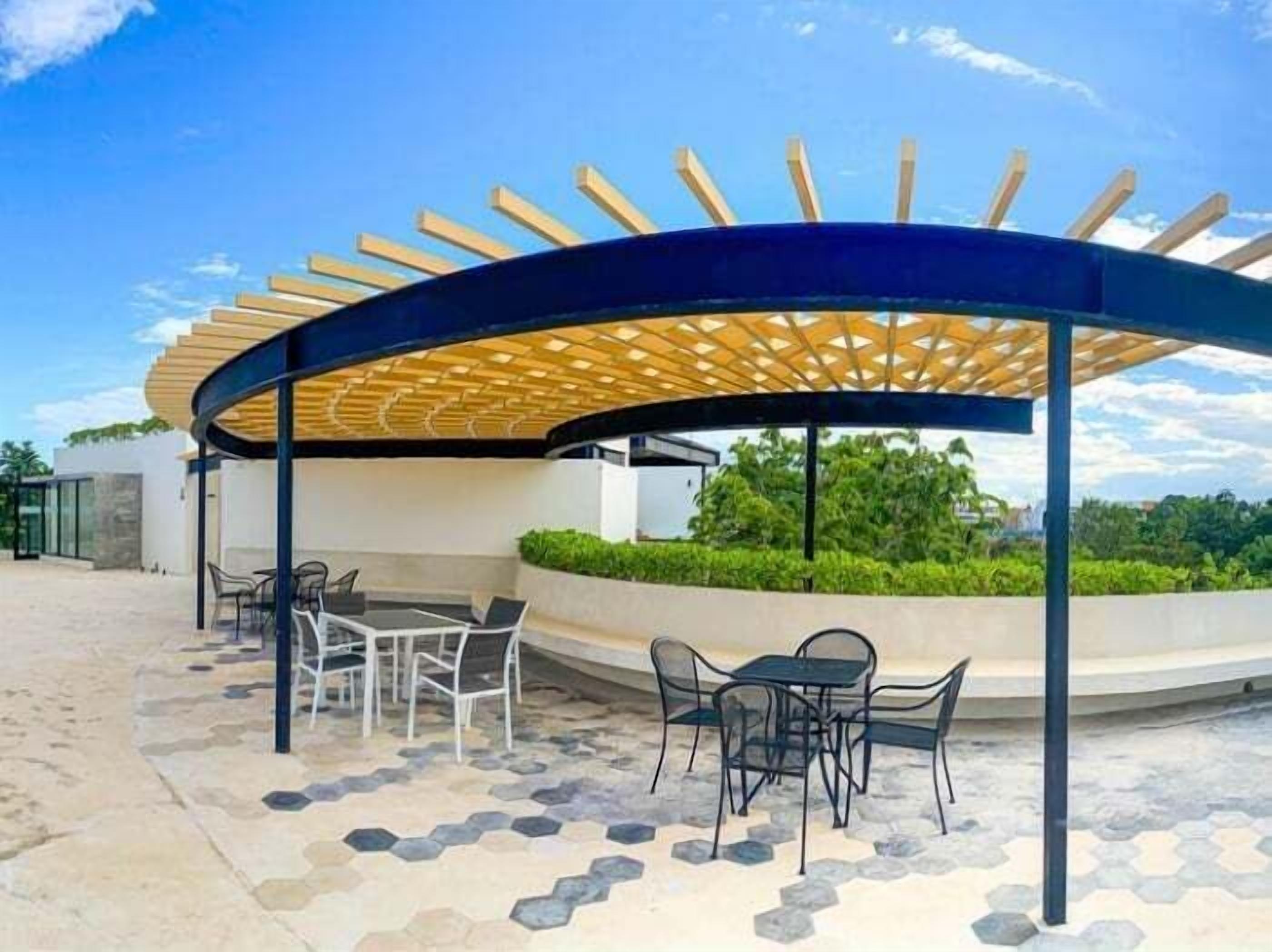 An outdoor seating area with a wooden pergola, hexagonal patterned flooring, and modern chairs.