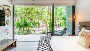 Un dormitori modern amb un llit gran, una televisió i vista a un jardí exuberant a través d'una porta de vidre.