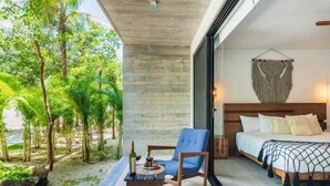 Un dormitori modern amb un llit gran, una cadira blava i vista a un jardí tropical.