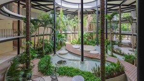 Un atrium à plusieurs niveaux, doté d’un élément aquatique central, entouré d’une végétation luxuriante et agrémenté d’espaces de détente modernes.