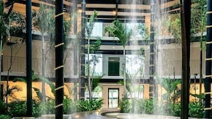 Un atrio de varios niveles con una fuente central, rodeado de vegetación y arquitectura moderna.