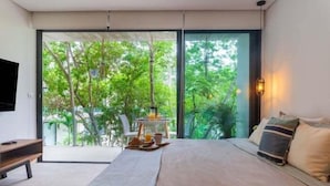 Un dormitorio con una cama grande, televisión, espacio para el desayuno y vistas a la vegetación.