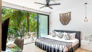 A modern bedroom with a large bed, a ceiling fan, and a view of a tropical garden. - 203D PANOR, Large Studio Pool 360° (Tulum)
