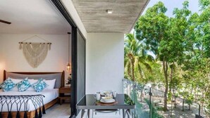 A modern bedroom with a large bed, bedside table, and a balcony with a glass railing overlooking a tropical garden. - 204B PANOR, Charming Studio! 360° Pool (Tulum)