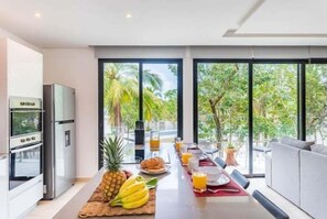 A modern kitchen with a dining area, large windows, and a view of greenery. - 205C PANOR, Large Apartment with 360° Pool (Tulum)
