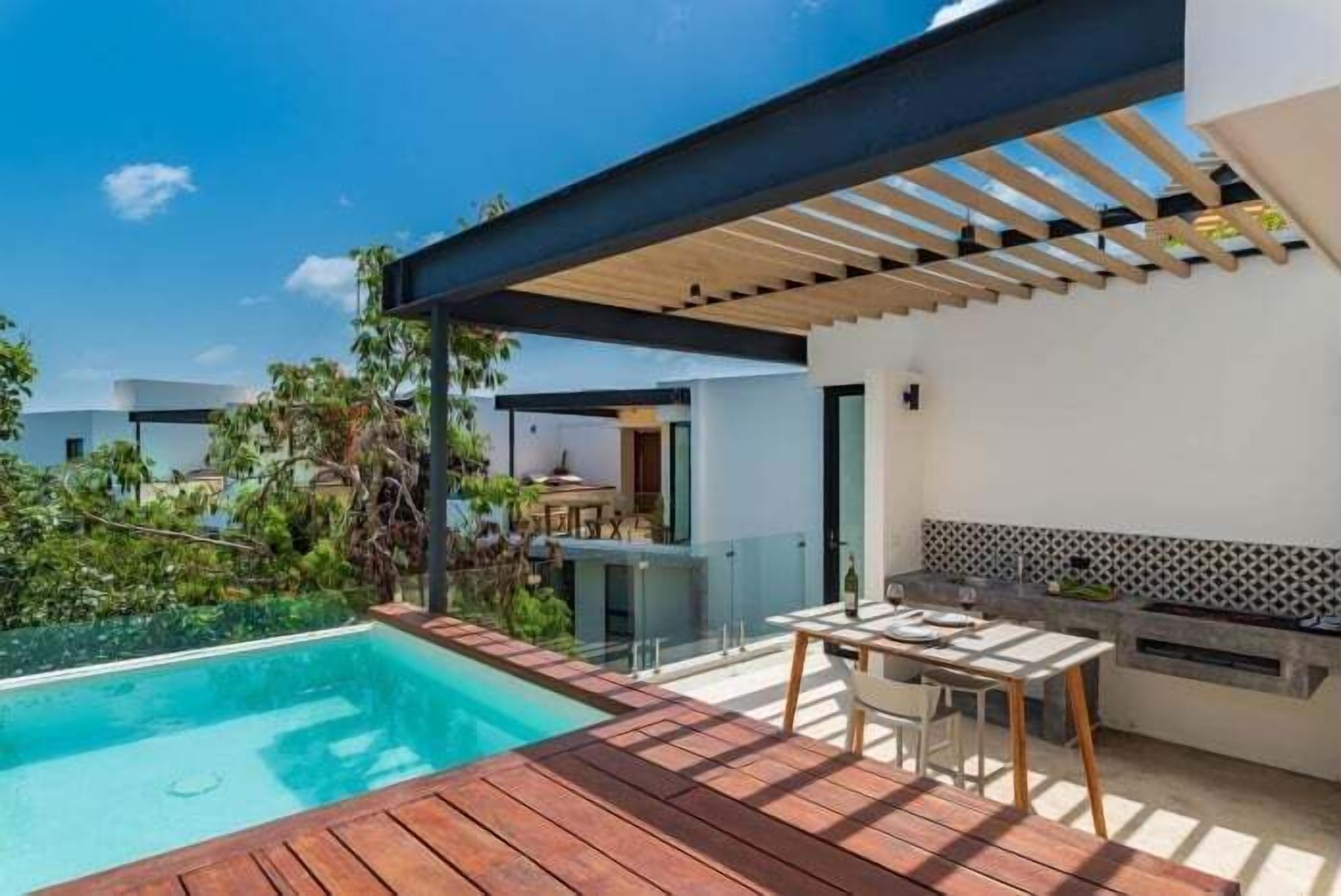 Un espace piscine extérieur moderne, doté d’une terrasse en bois, d’une table et d’un barbecue.