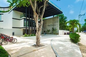 A modern building with a covered entrance, a tree in the foreground, and a clear sky. - PH8C PANOR, Luxury Penthouse Alberca Privada (Tulum)
