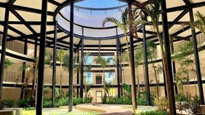 A multi-level atrium with a central glass dome, surrounded by palm trees and a curved wooden bench. - PH8C PANOR, Luxury Penthouse Alberca Privada (Tulum)
